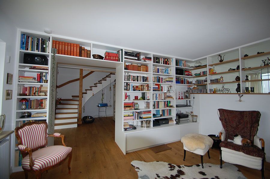 Eingebaute Regalwand die über dem Durchgang verläuft und die Wand entlang mit vielen Büchern