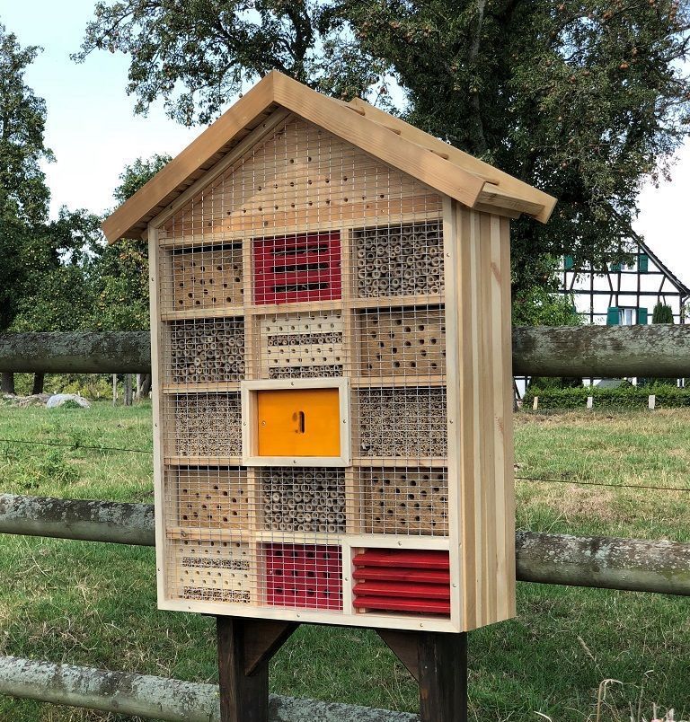 Insektenhotel aus Holz mit abschraubbarer Metall-Gitterfront zum Schutz vor Vögeln. Aufgestellt vor einem Holzzaun