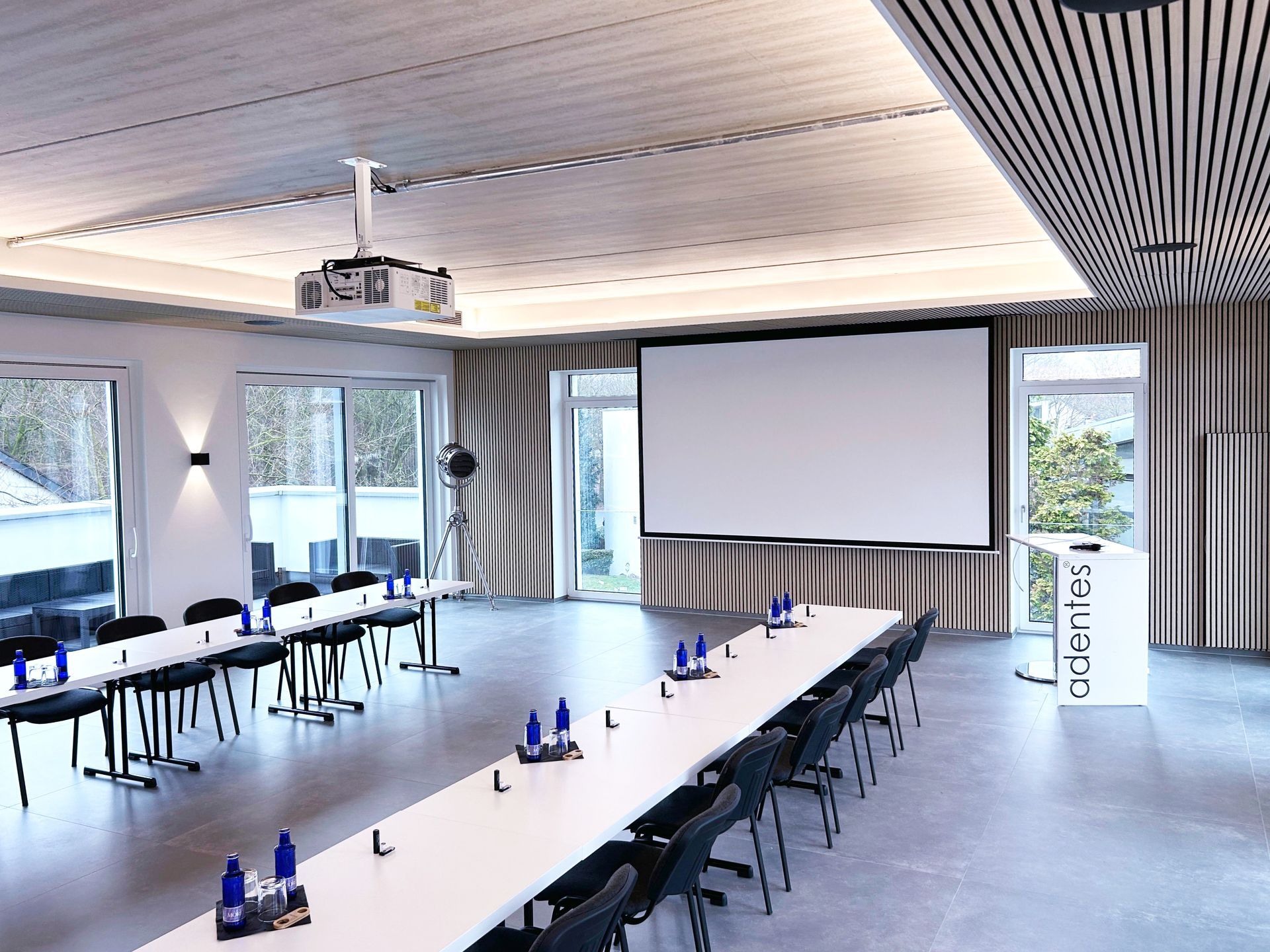Konferenzraum mit langen Tischen, Projektionsleinwand und Stuhlreihen.