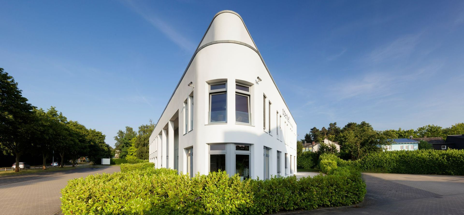 Ein weißes Gebäude ist von Bäumen und Büschen umgeben