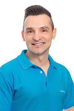 MSc Implantologie & Parodontologie Eine Mann in einem blauen Poloshirt lächelt in die Kamera.
