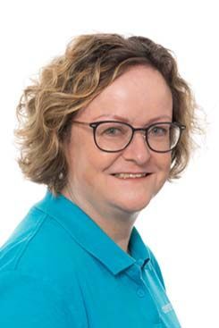 Unser Rezeptionsteam Eine Frau mit Brille und blauem Hemd lächelt in die Kamera.
