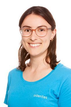 Eine Frau mit langen dunklen Haaren trägt ein blaues Hemd und eine Halskette.