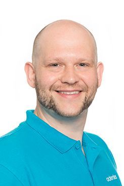 Physiotherapeut Ingolf Ein kahlköpfiger Mann mit Bart trägt ein blaues Hemd und lächelt.
