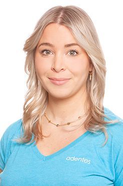 Eine Frau mit langen Haaren trägt ein blaues Hemd und lächelt.