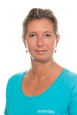 Fachzahnärztin - Oralchirurgie Eine Frau mit blauem Hemd und Ohrringen steht vor einem weißen Hintergrund.