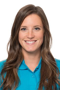Physiotherapeutin Lara Eine Frau mit langen braunen Haaren trägt ein blaues Poloshirt und lächelt.