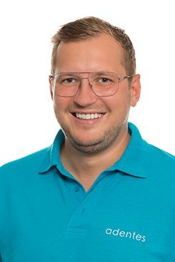 Arzt für Oralchirurgie & Implantologie Ein Mann mit Brille und blauem Hemd lächelt in die Kamera.