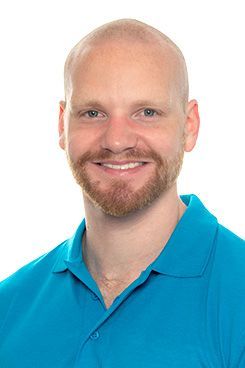 Ein kahlköpfiger Mann mit Bart trägt ein blaues Poloshirt und lächelt.