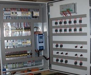 Panel de control eléctrico con cables, interruptores y componentes. Armario metálico gris abierto, con cableado complejo a la vista.