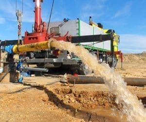 Equipo de perforación de pozos expulsando agua a una zanja en un entorno desértico; cielo despejado.