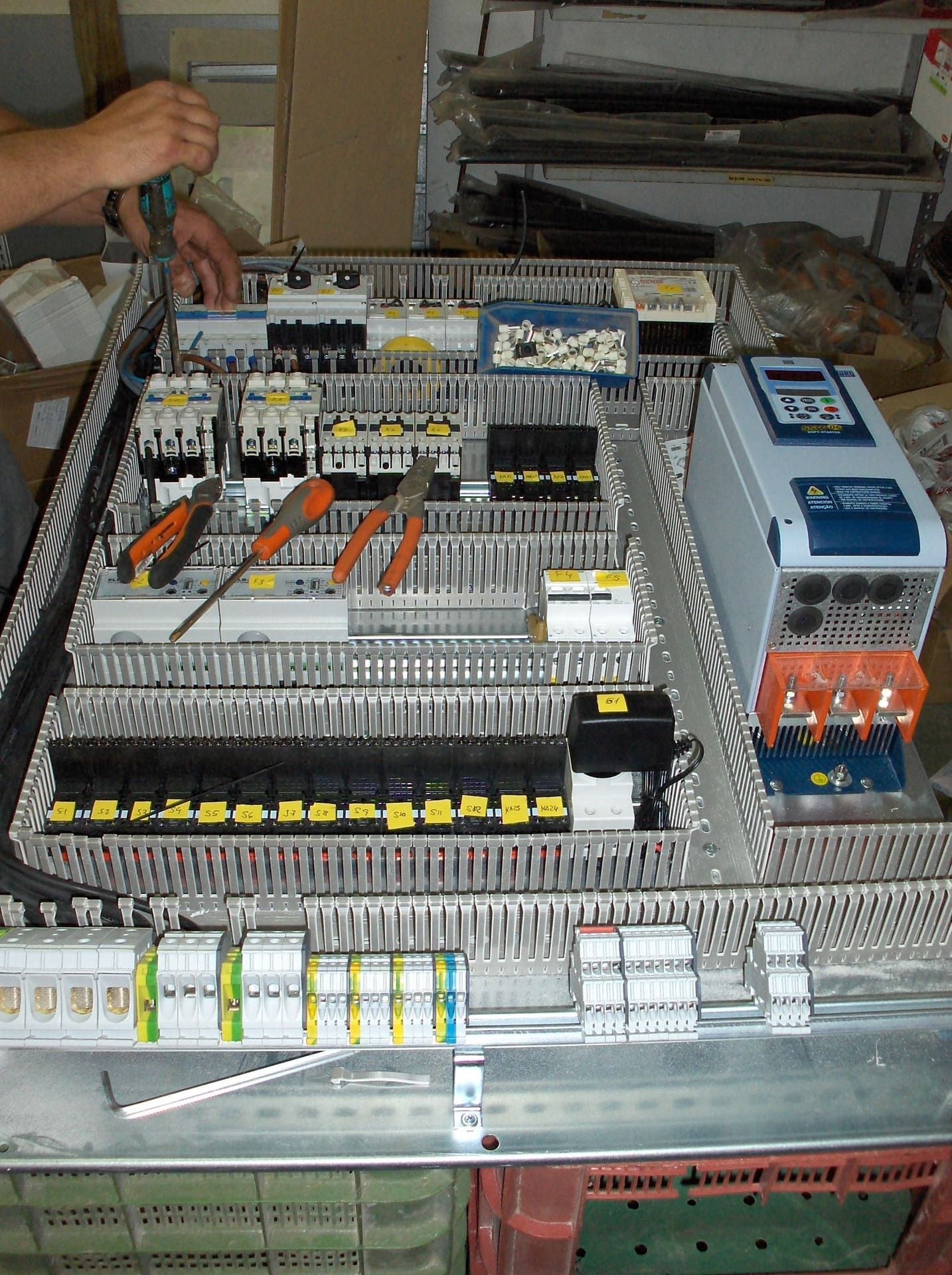 Se está ensamblando un panel eléctrico; se ven las herramientas y los componentes; hay una persona trabajando.