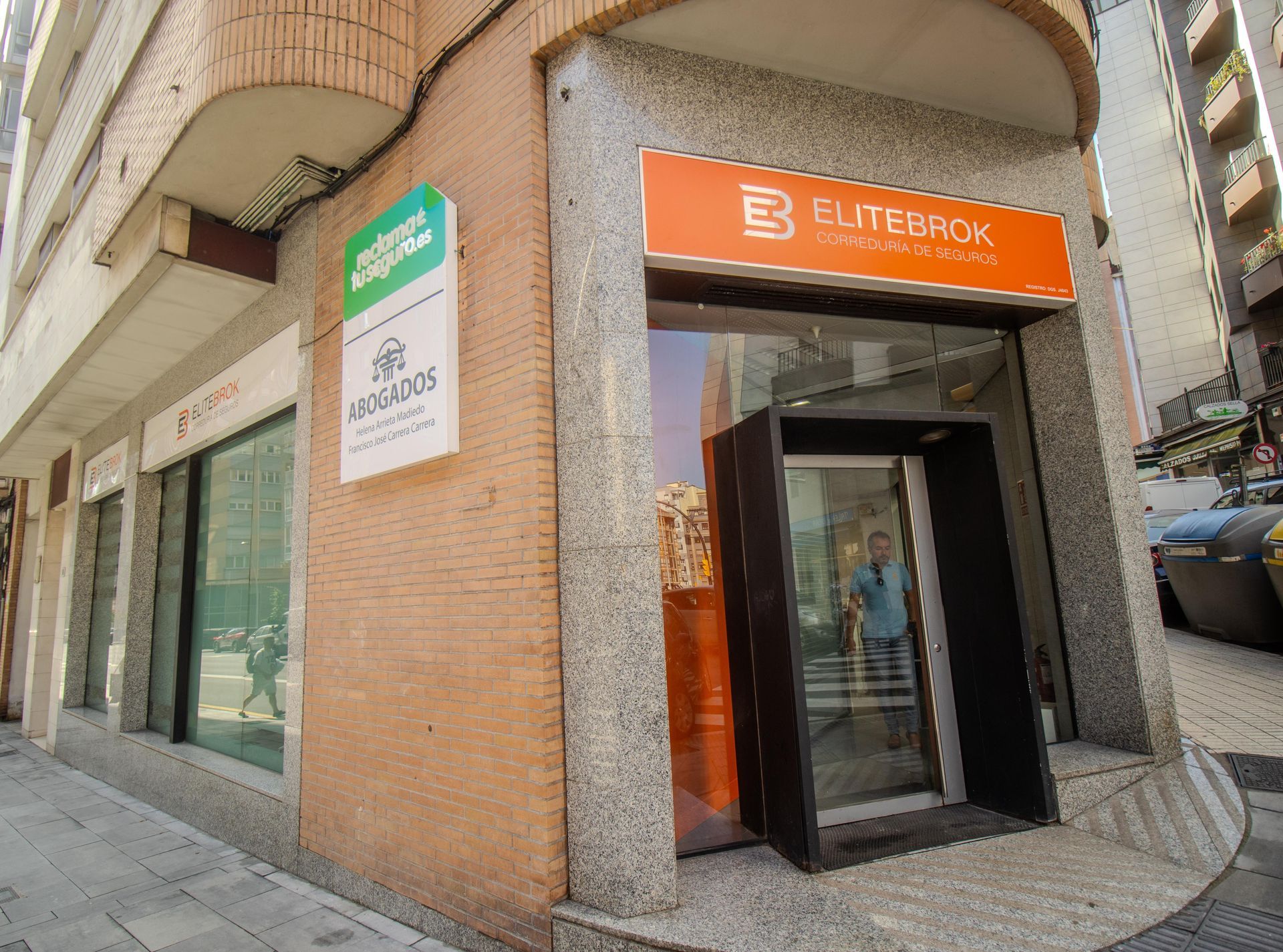 Entrada de una tienda naranja en una esquina de una calle, con puertas de cristal y letreros sobre la entrada