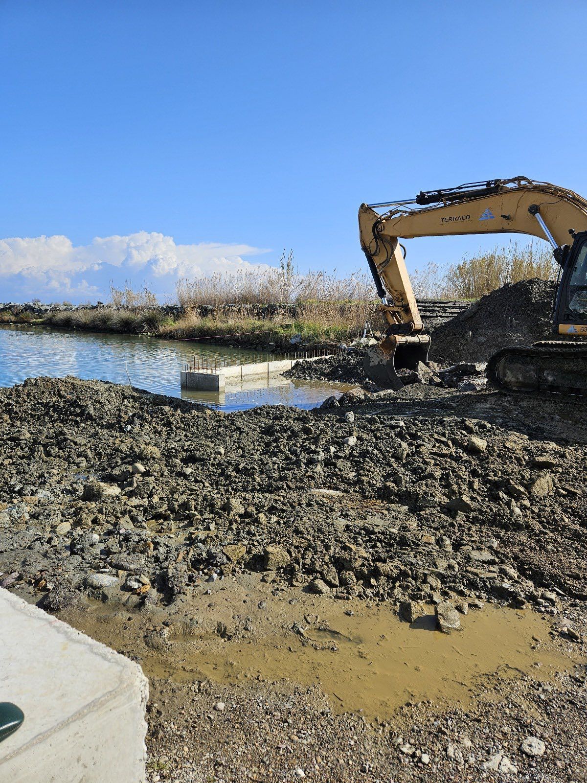 Une excavatrice extrait de la terre du bord d'une étendue d'eau