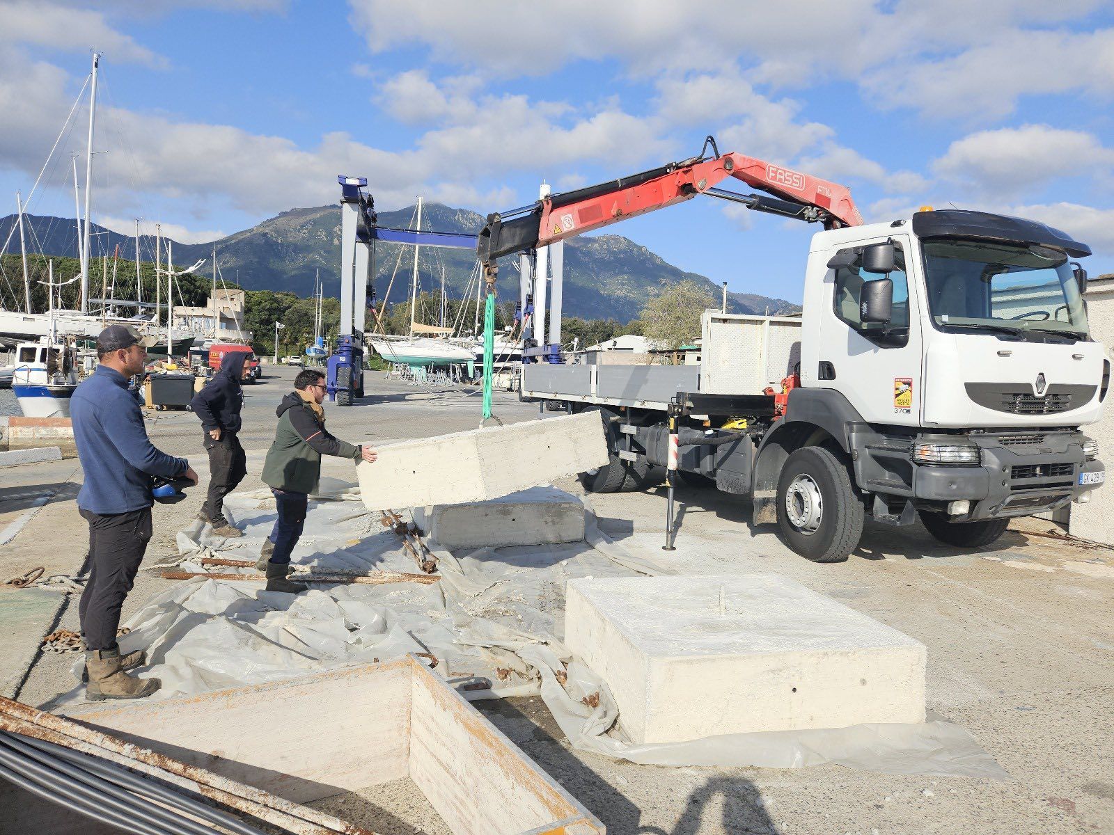 Des ouvriers utilisent une grue pour déplacer des blocs de béton dans un port de plaisance