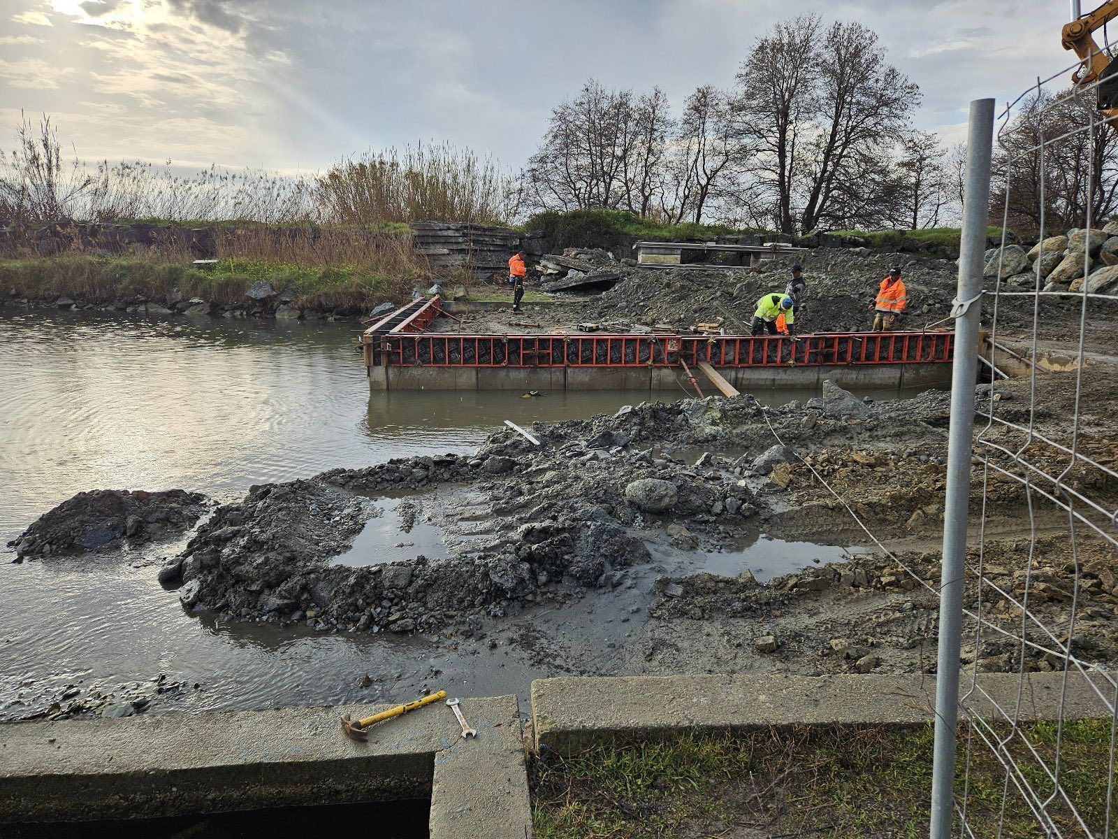 Chantier de construction au bord de l'eau : ouvriers, coffrage, boue et ciel couvert