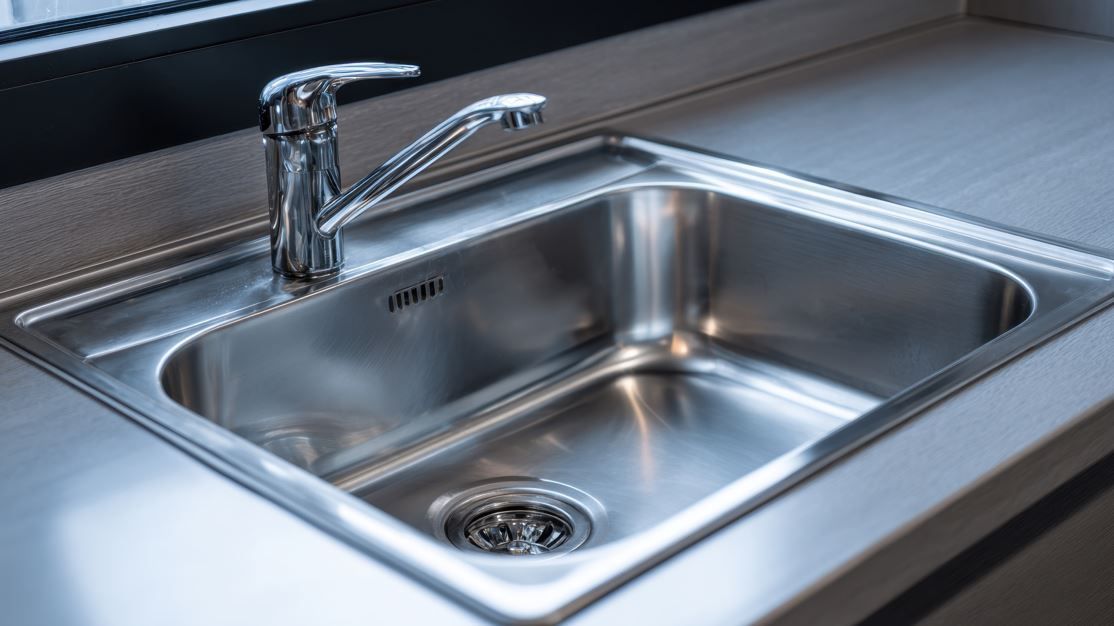 Fregadero de cocina de acero inoxidable con grifo, colocado en una encimera de color claro.