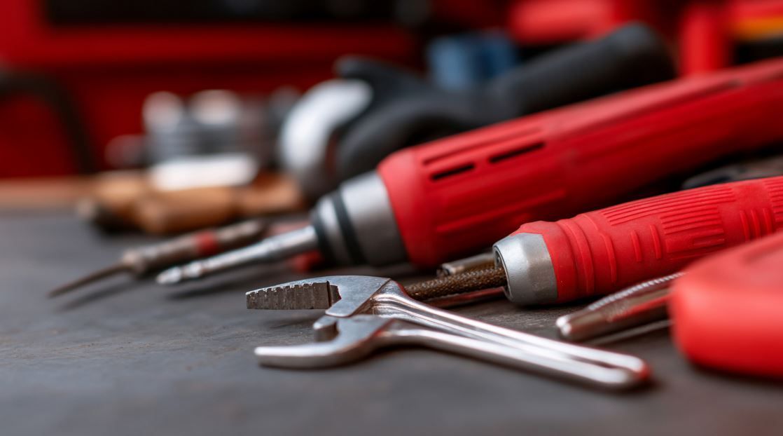 Primer plano de herramientas: destornillador rojo, llave inglesa y otras sobre una superficie oscura.