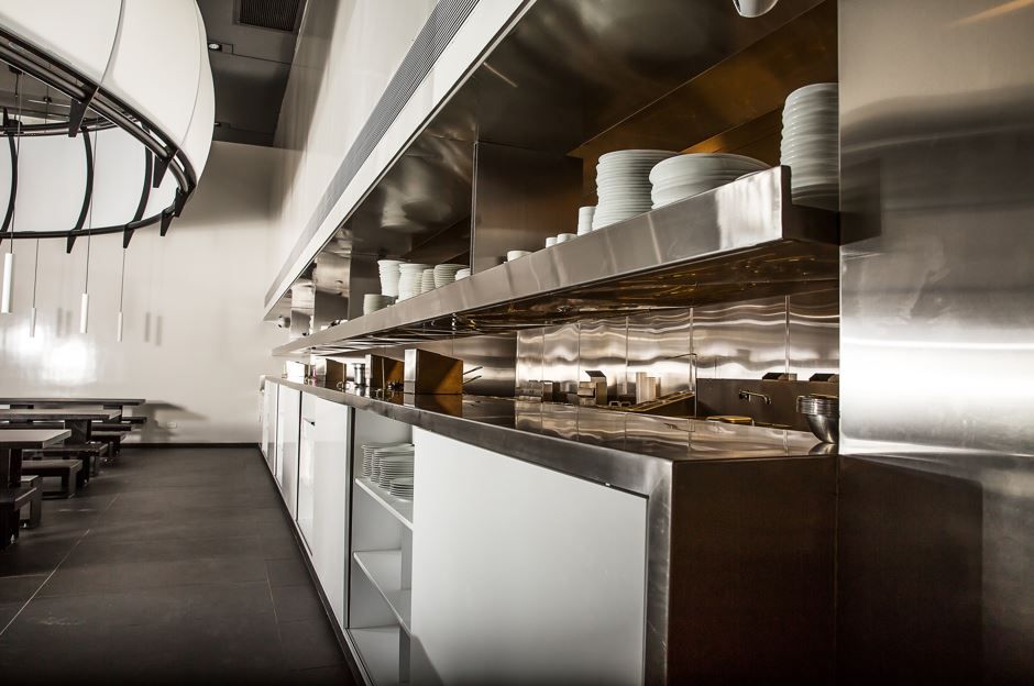 Trabajador de control de plagas con traje protector rociando el piso de una cocina, con insectos marrones cerca.