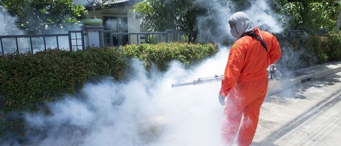 Un hombre con un mono naranja está rociando humo en una calle.
