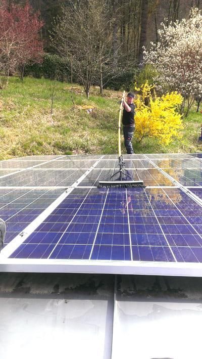 Ein Mann reinigt ein Solarpanel mit einem Besen.