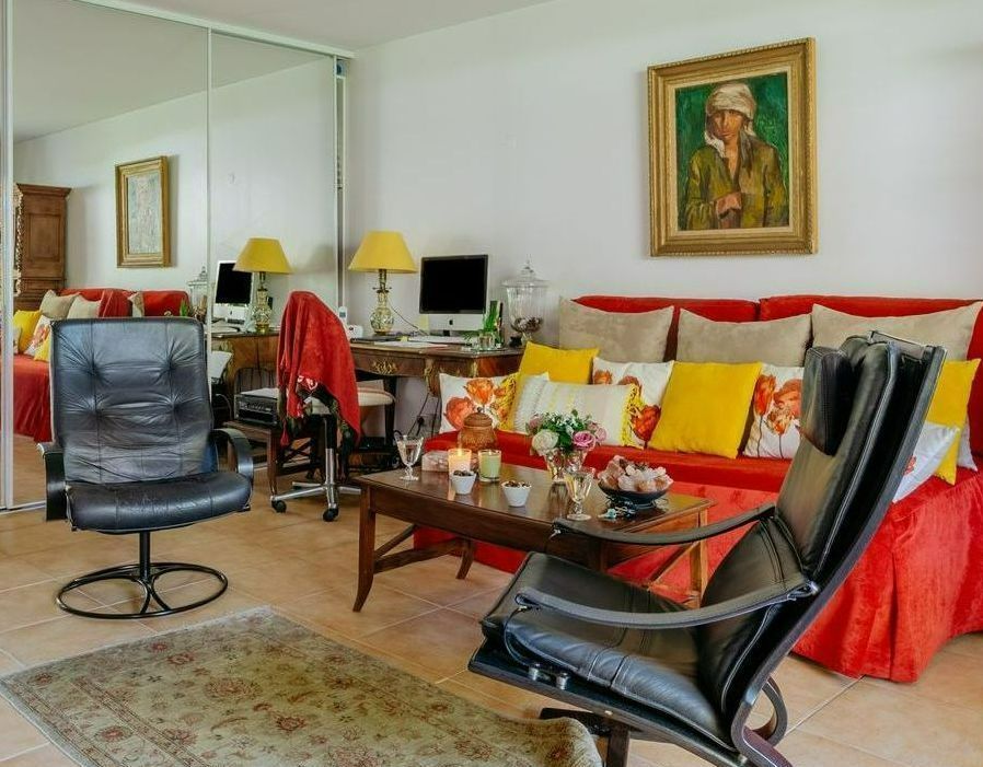Salon avec canapé rouge, fauteuils noirs, table basse en verre, miroirs et un tableau au mur.