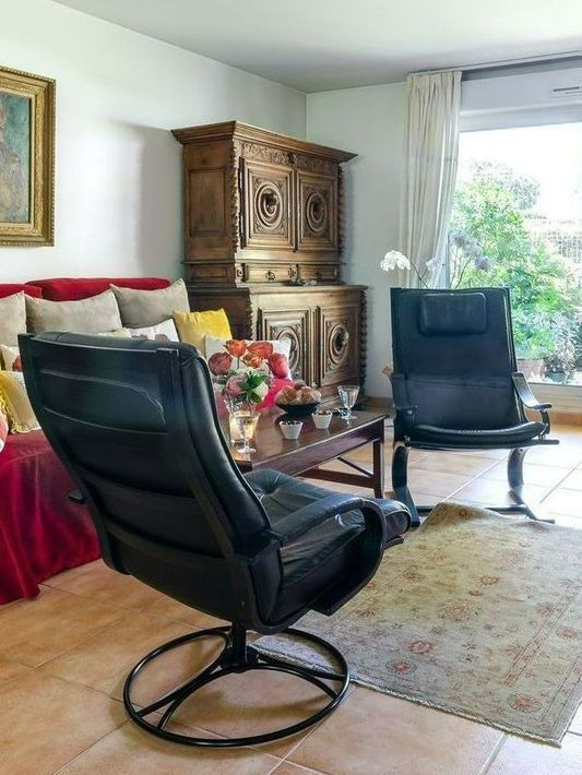 Salon avec deux fauteuils pivotants noirs, un tapis beige, un canapé et un meuble en bois près d'une fenêtre lumineuse.