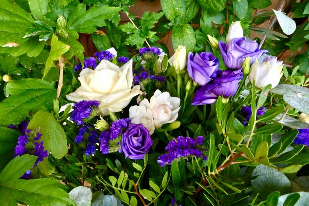 Des roses et des fleurs violettes et blanches disposées au milieu d'un feuillage vert.