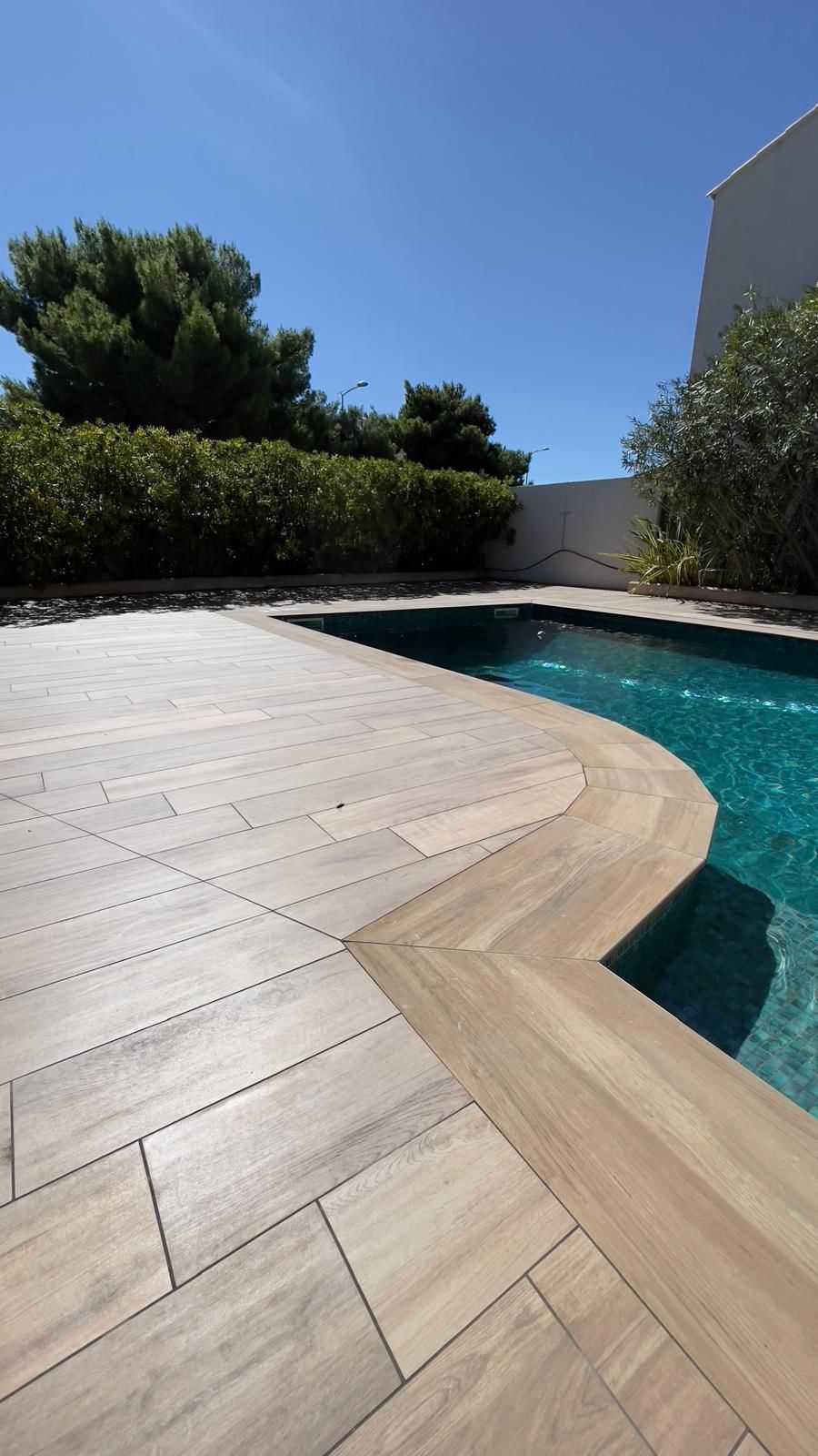 Au bord de la piscine, des carreaux de bois clair, une eau turquoise et un ciel d'un bleu limpide.