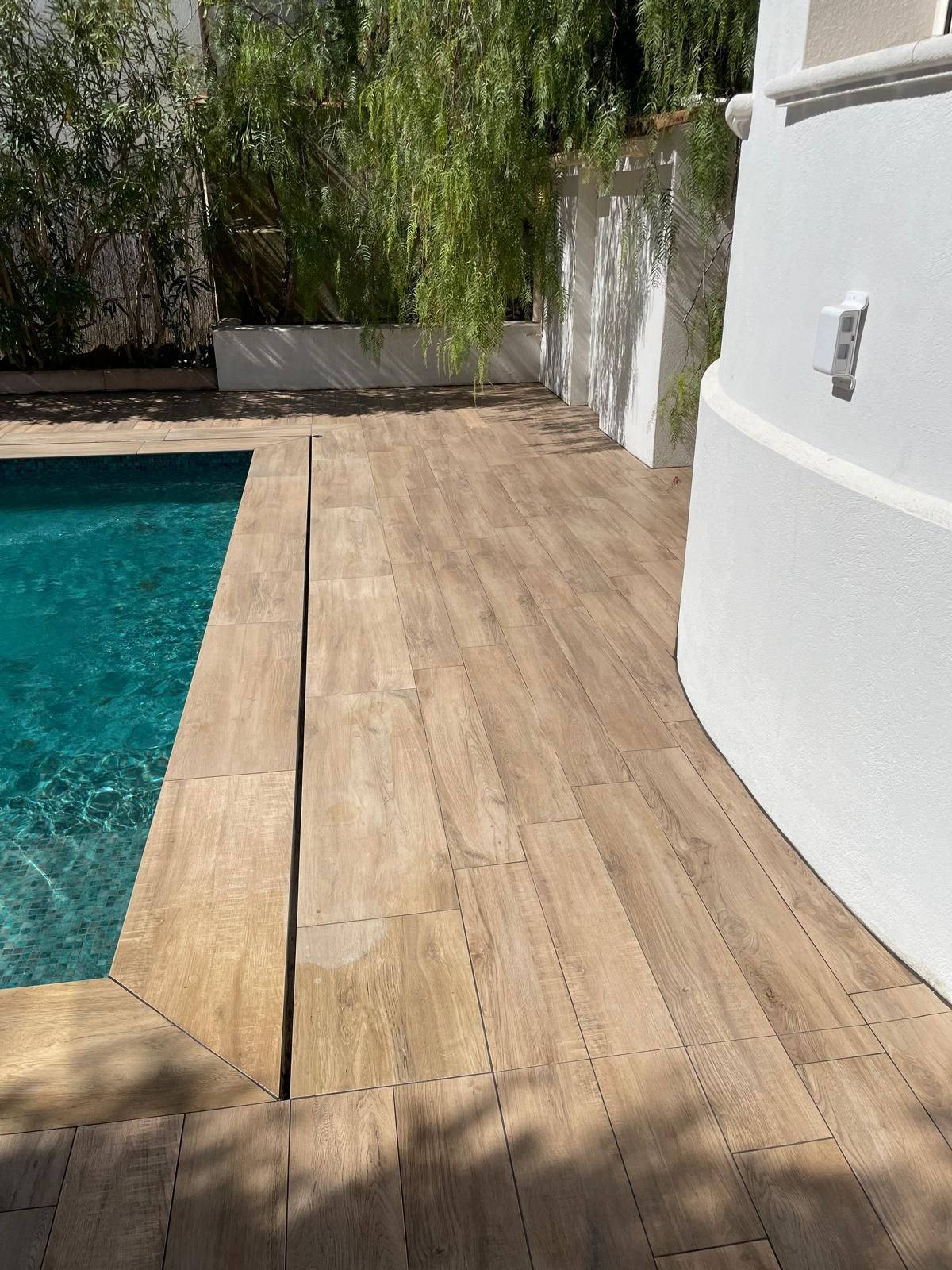 Terrasse de piscine carrelée façon bois, bordant une piscine turquoise.