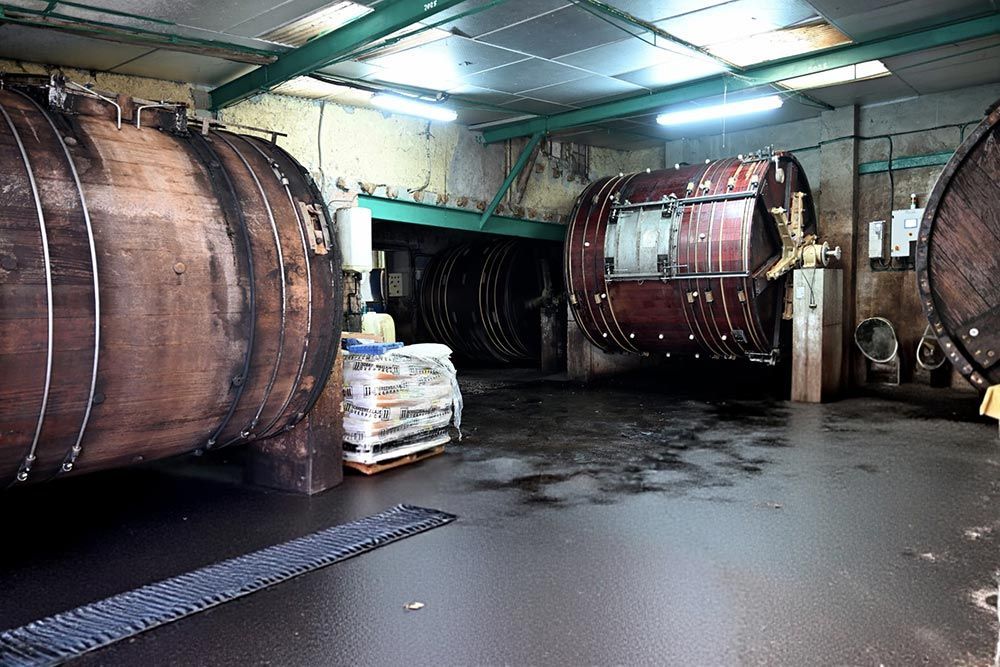 Habitación industrial oscura con enormes barriles de madera y suelo de hormigón mojado bajo luces fluorescentes.