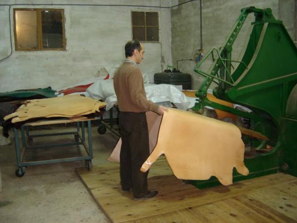 Un hombre sostiene un trozo de cuero delante de una máquina.