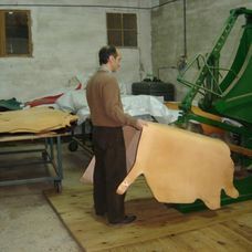 Un hombre está de pie junto a un gran trozo de cuero en una fábrica.