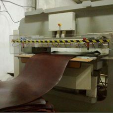 Máquina industrial que introduce una ancha lámina marrón a través de un dispositivo de taller con barra de seguridad.
