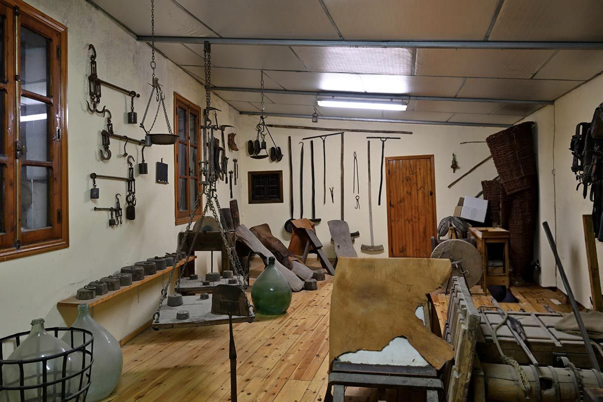 Interior de un taller con herramientas colgadas en las paredes, bancos de trabajo y trozos de madera esparcidos por el suelo.