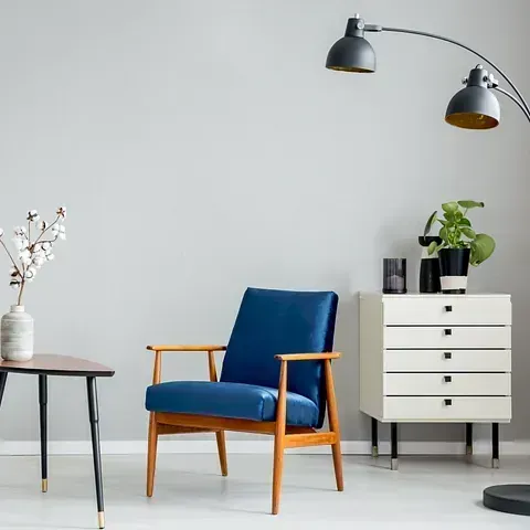 Una sala de estar con una silla azul, una lámpara, una mesa y una cómoda.