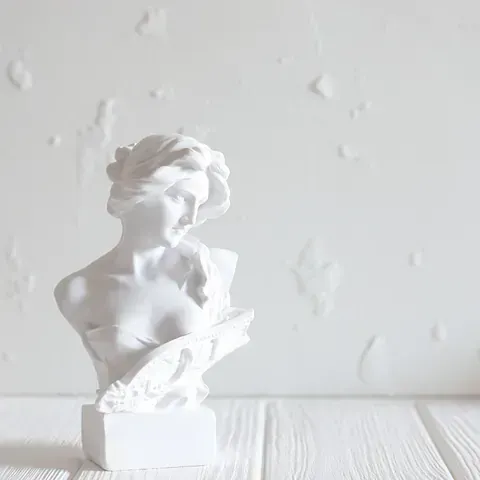 Una estatua blanca de una mujer está sentada en una mesa de madera blanca.