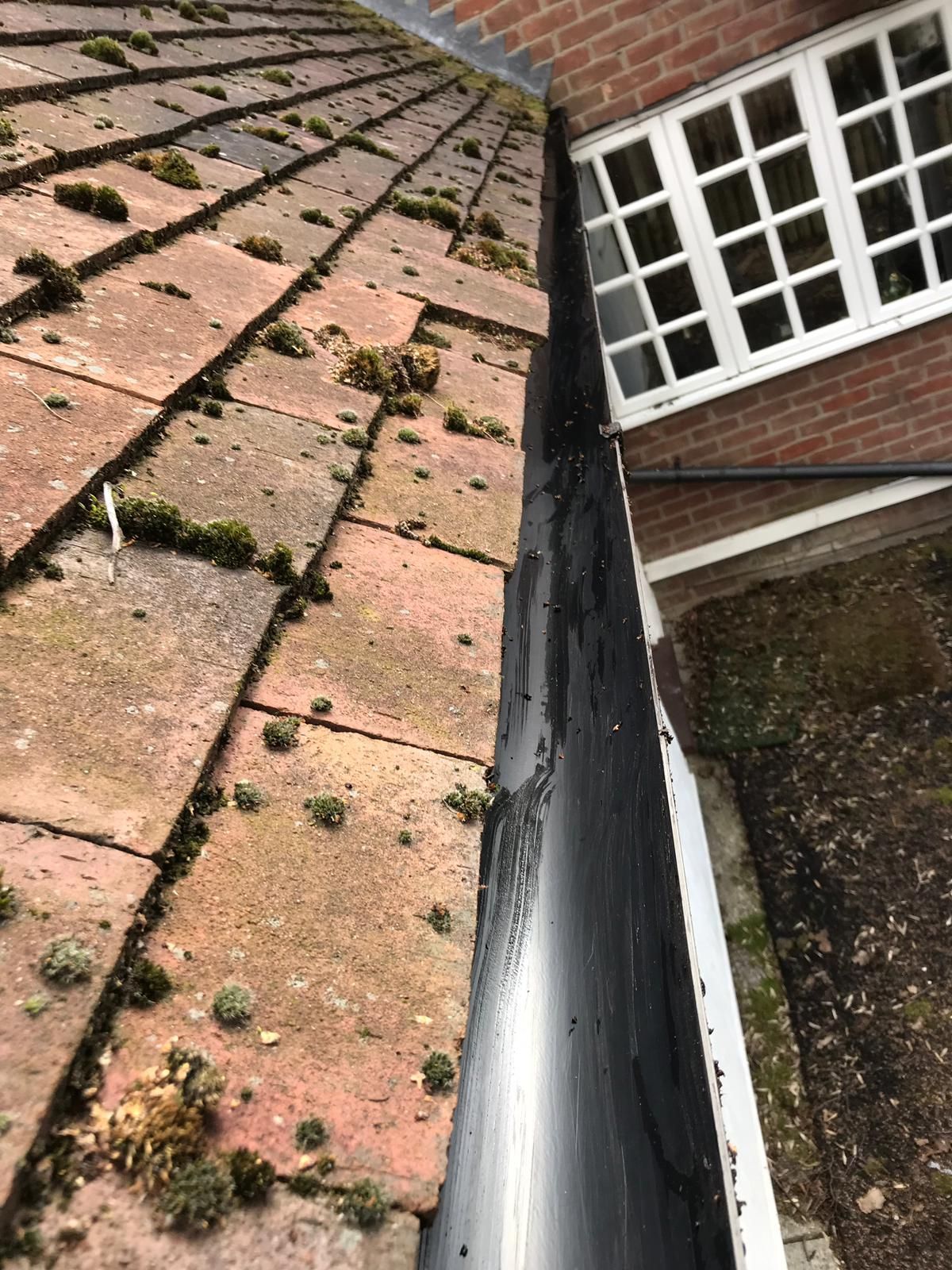 Roof gutter between mossy red tiles and a brick wall with a white window