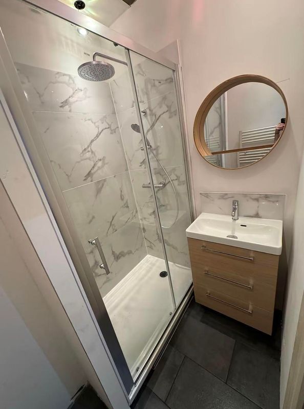 Petite salle de bains avec douche vitrée, miroir mural et meuble-lavabo blanc avec vasque.