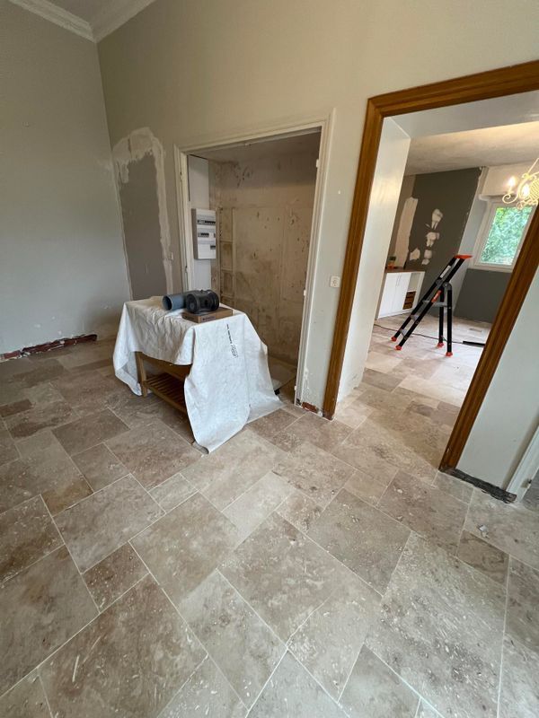 Pièce vide avec un sol carrelé beige, des portes ouvertes et une table recouverte sur laquelle se trouve un petit appareil.