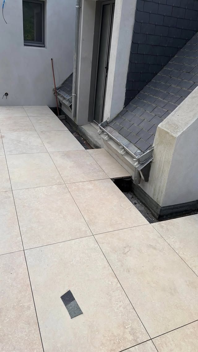Allée extérieure carrelée longeant un bâtiment, avec une rampe surélevée et un seuil étroit