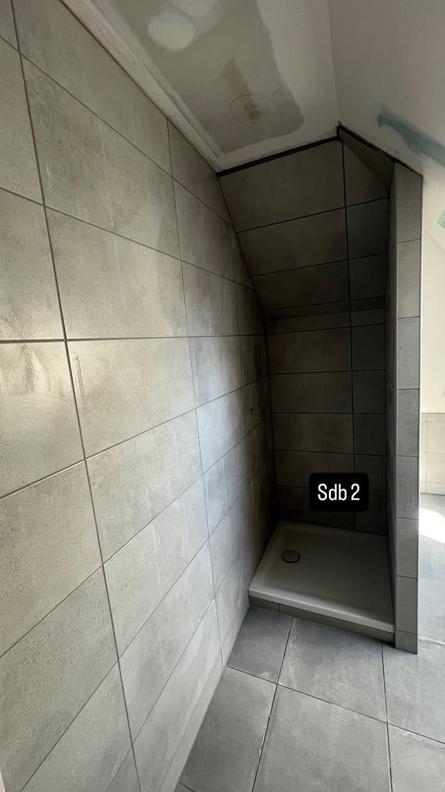 Petite cabine de douche carrelée, étroite, avec une marche et une ouverture sombre au fond