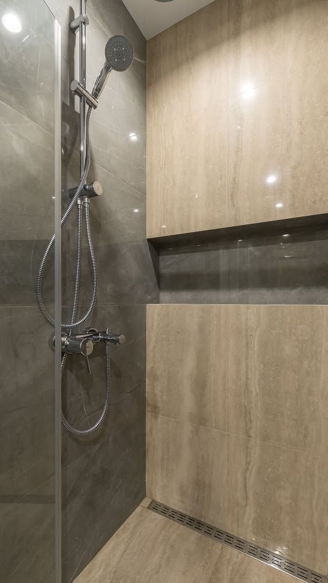 Cabine de douche moderne avec douchette à main, panneaux muraux imitation bois et bordure de sol en galets