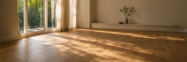 Pièce vide baignée de soleil, avec un parquet en bois, des rideaux transparents et un petit vase posé sur l’étagère murale