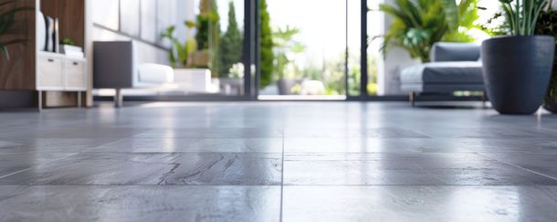 Salon moderne avec sol carrelé, canapé, plante en pot et grandes portes vitrées donnant sur l’extérieur
