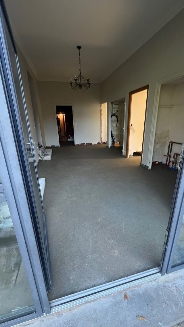 Salon vide avec moquette, vu depuis une porte ouverte, avec des murs blancs et un plafonnier.