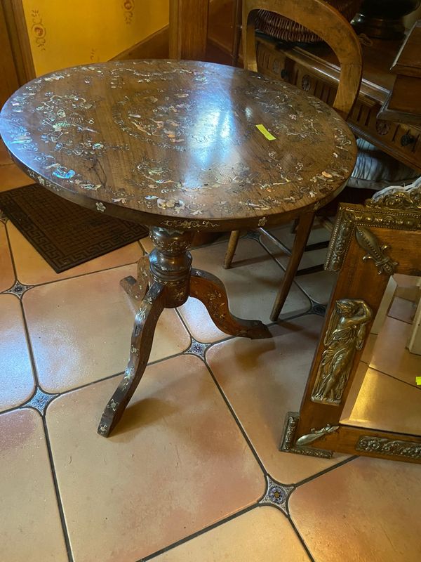 Une table ronde sur pied, à plateau de marbre brun, se dresse sur un sol carrelé, à côté d'un meuble en bois orné de détails dorés.