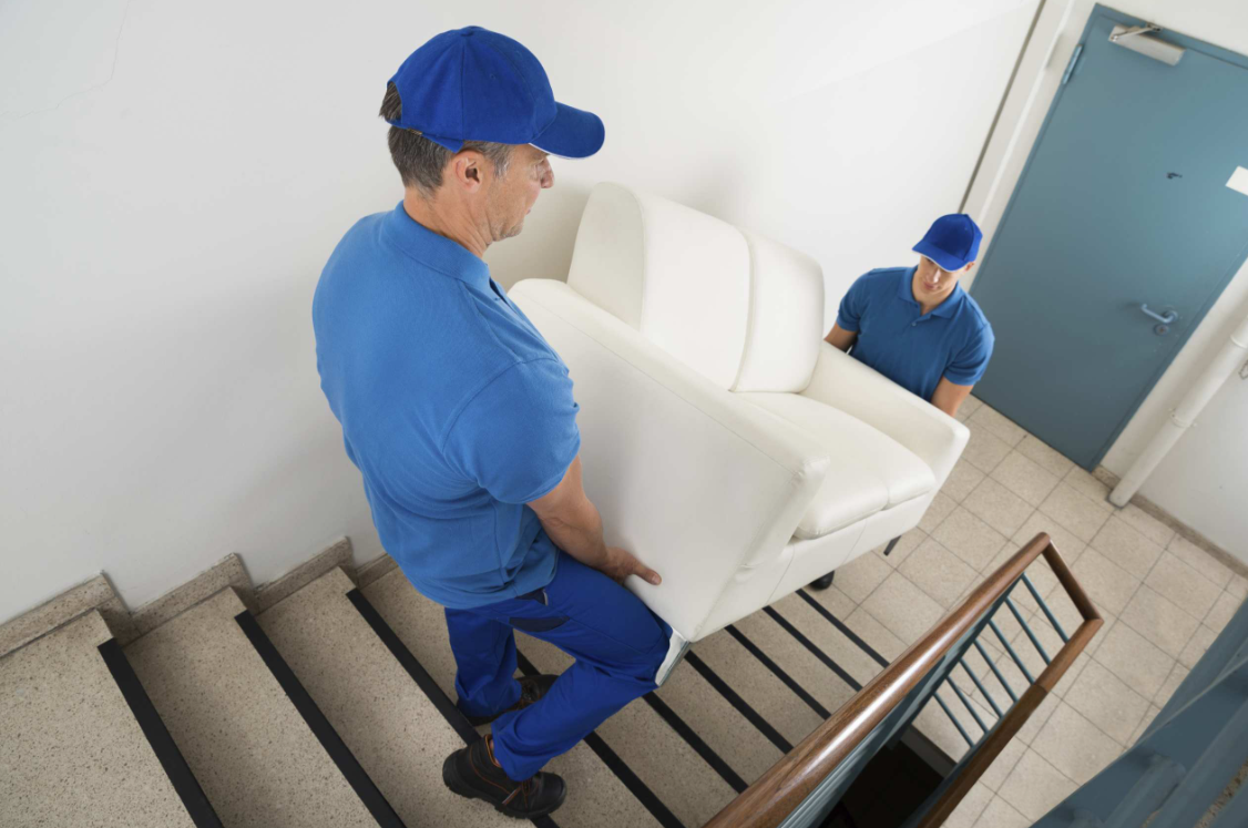 Dos trabajadores de mudanzas suben un sofá blanco por las escaleras de una casa