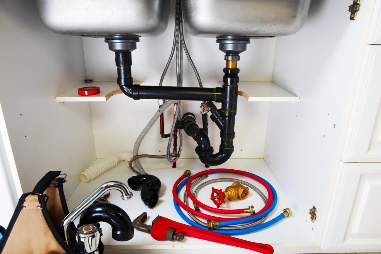 Instalación de fontanería bajo el fregadero con dos lavabos de acero inoxidable, tuberías expuestas