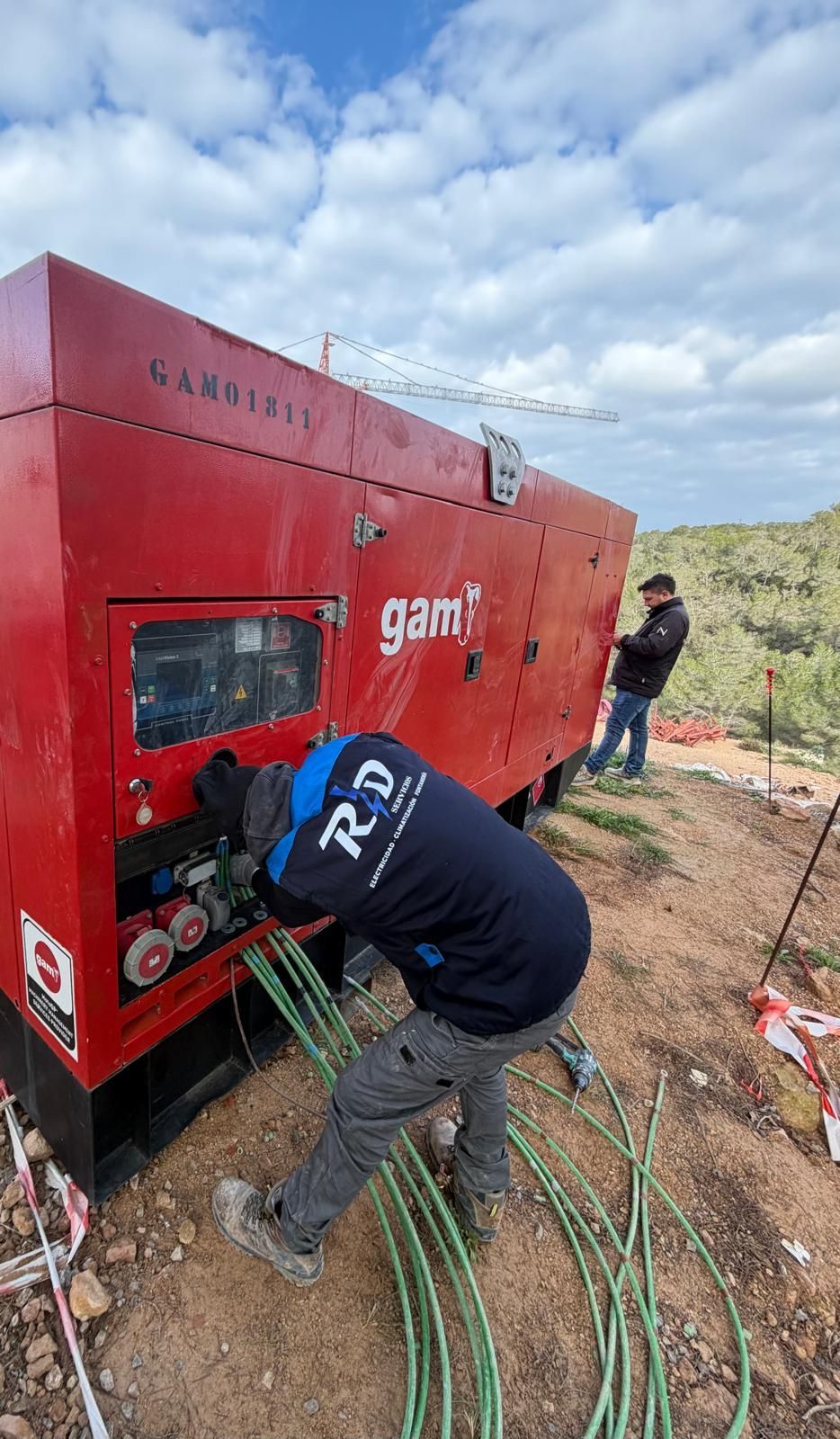Dos trabajadores manejan una gran máquina roja al aire libre bajo un cielo nublado.